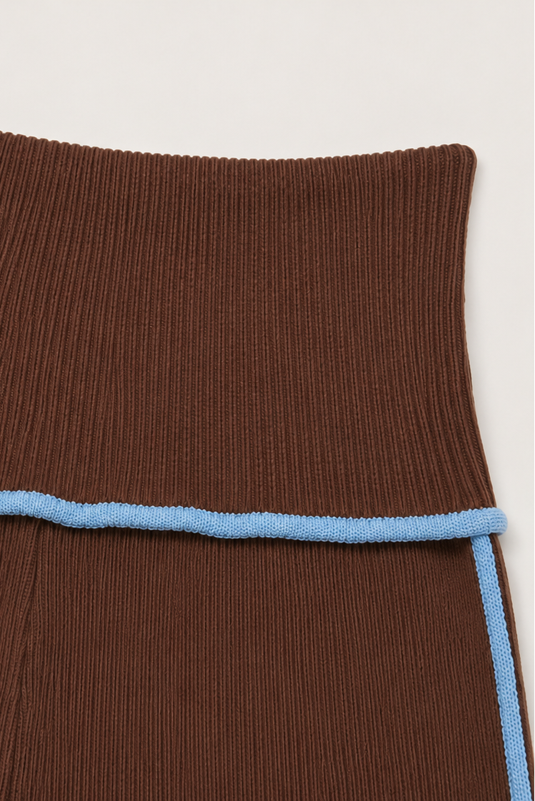 Close-up of a ribbed brown knit garment, likely a skirt or dress, featuring a light blue contrast trim running horizontally and vertically along the side seams.